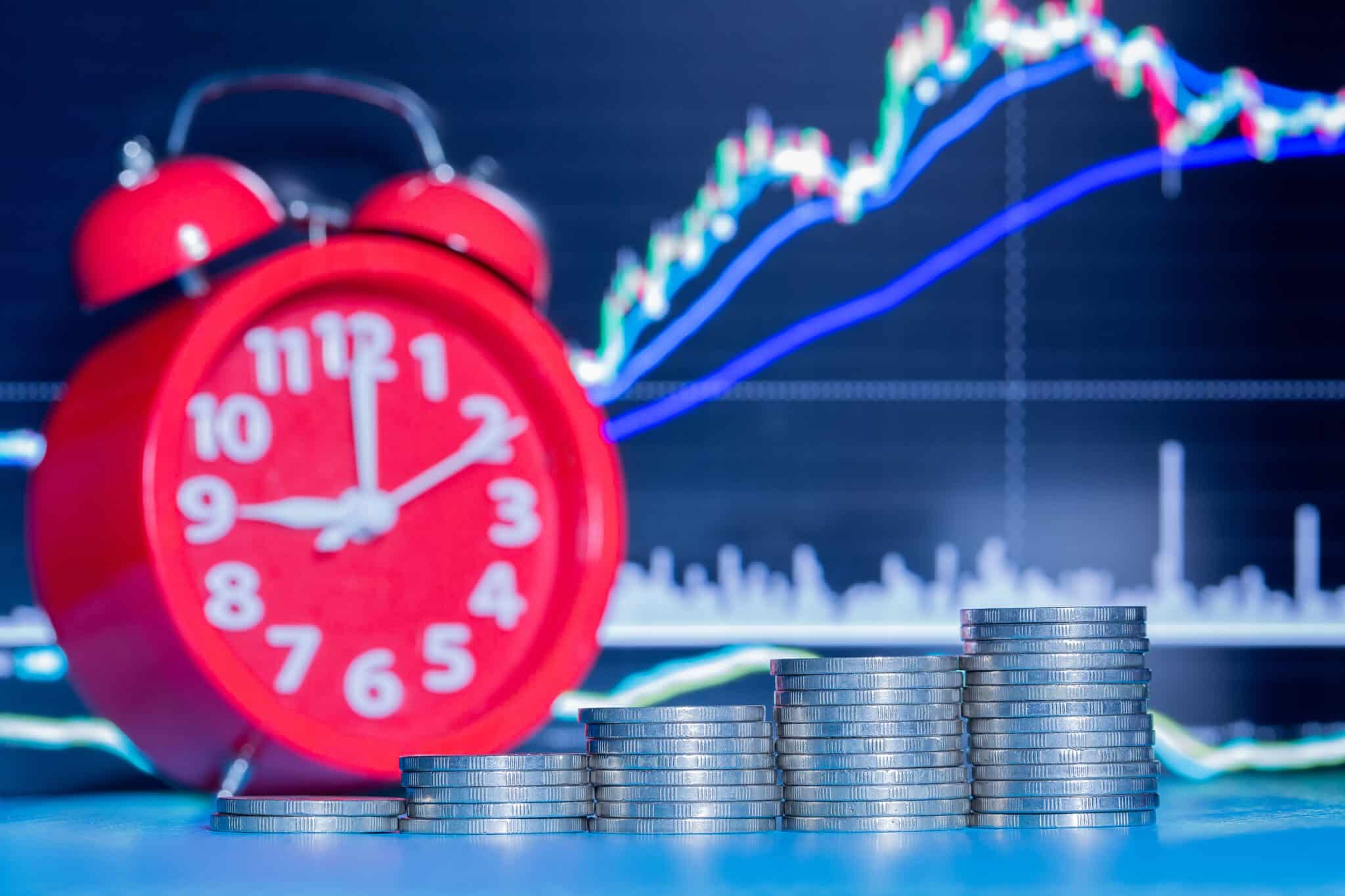 A stack of five rows of coins and an alarm clock, with a dark blue graph