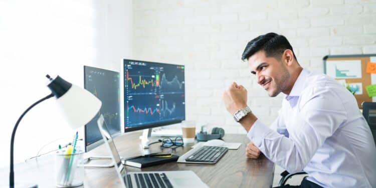 Confident handsome Hispanic financial broker showing fist to computer screen while trading from home